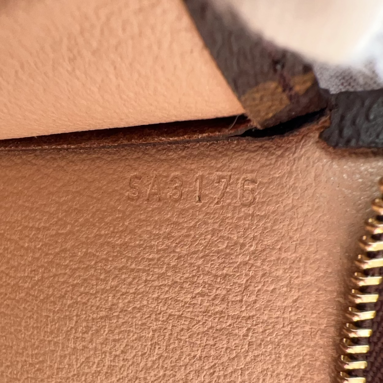 Close-up of a brown leather bag with gold zipper and visible brand stamp.