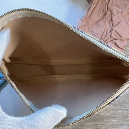 A close-up of a beige zippered pouch or cosmetic bag being held open by a white gloved hand, with a light-colored fabric surface and a pink crumpled paper visible in the background.