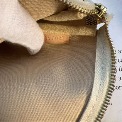 Close-up of a beige canvas zippered pouch or bag interior with a tan leather label reading 'CA 5027' and a white fabric pull tab, photographed against printed paper with partial text visible.
