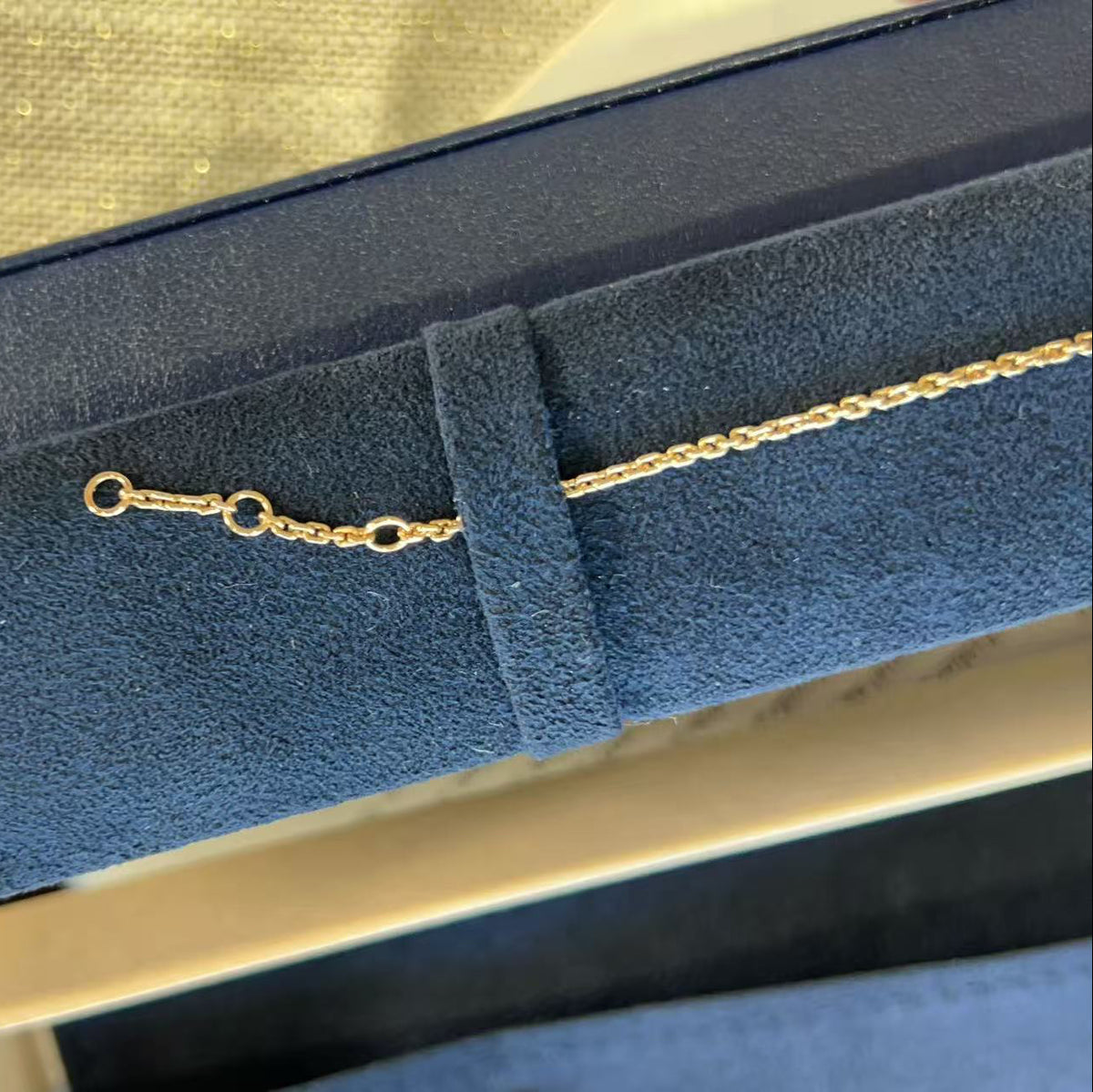 A close-up of a delicate gold chain necklace with an adjustable lobster clasp, resting inside a dark blue velvet jewelry box.