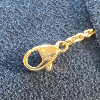 A close-up of a polished gold lobster clasp attached to a gold chain, resting on a textured dark gray fabric surface.