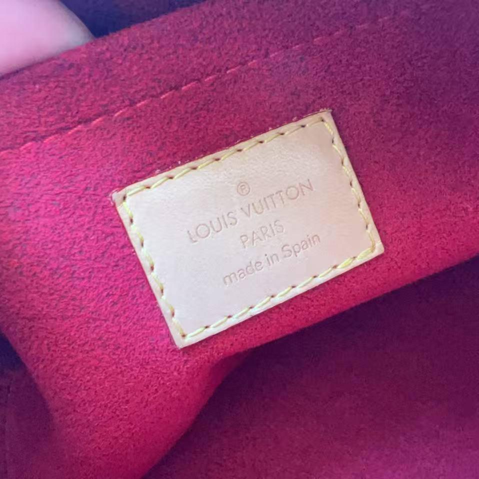 Close-up of a Louis Vuitton interior label stitched onto a deep red velvet or suede-like fabric, with fingers holding the fabric at the left edge.