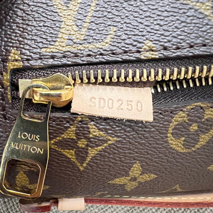 Close-up of a Louis Vuitton monogram zipper pouch showing the dark brown coated canvas with gold monogram print, a gold-tone zipper, and a white paper tag with the code SD0250.