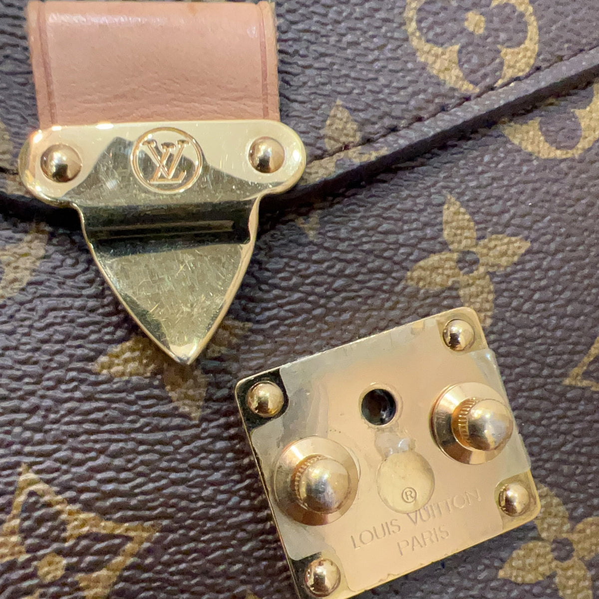 Close-up of a Louis Vuitton monogram bag showing a gold-tone lock clasp and a separate lock plate on a brown coated canvas with tan monogram print.