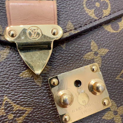 Close-up of a Louis Vuitton monogram bag showing a gold-tone lock clasp and a separate lock plate on a brown coated canvas with tan monogram print.