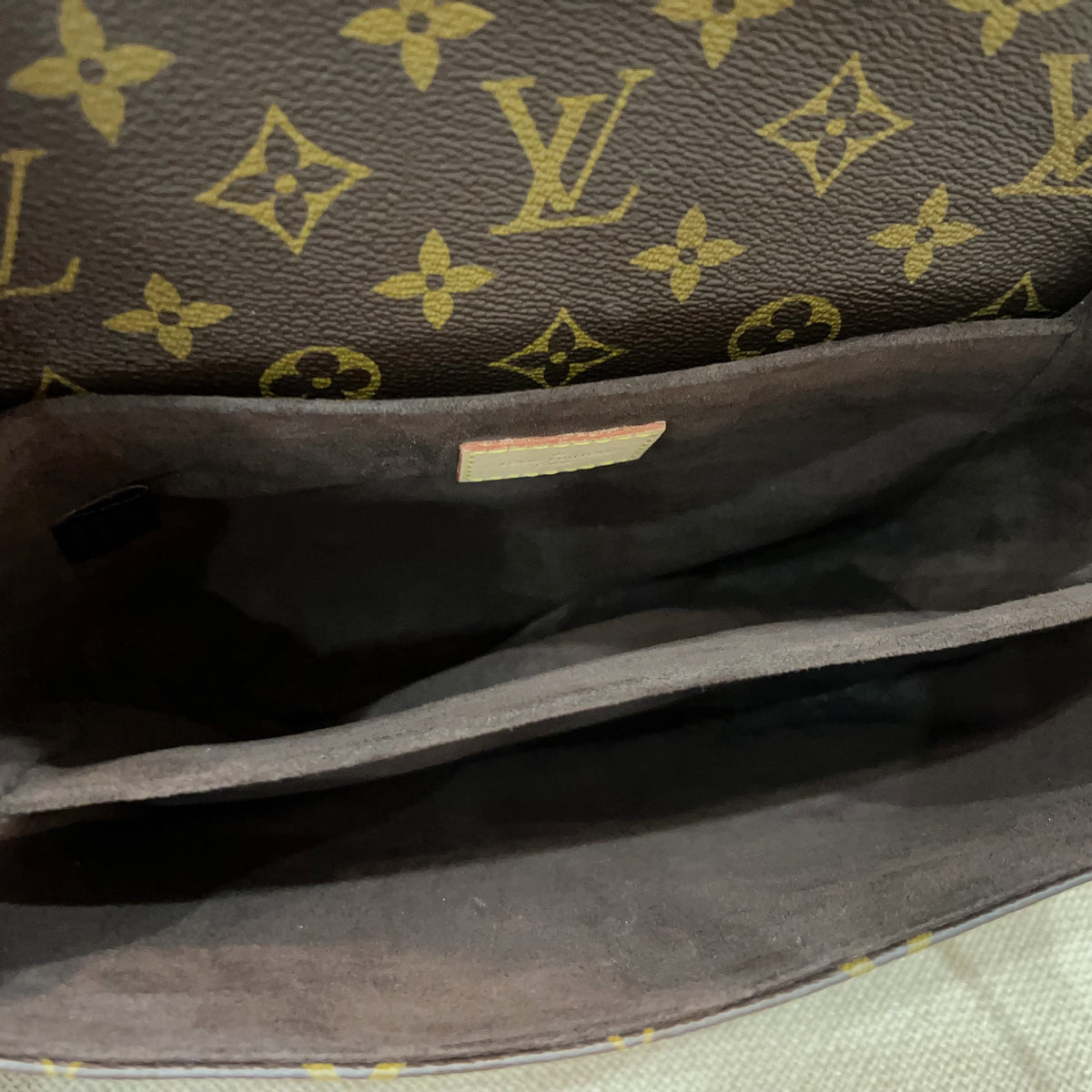 Close-up view of the interior of a Louis Vuitton handbag, showing the dark brown monogram canvas exterior and the dark gray suede or leather lining.