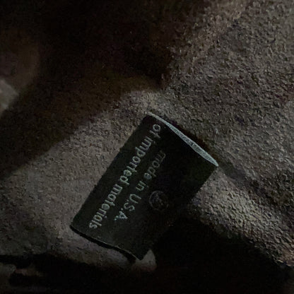 Close-up of a Louis Vuitton interior label stitched onto a dark brown fabric surface, with part of the classic monogram canvas visible at the top right.
