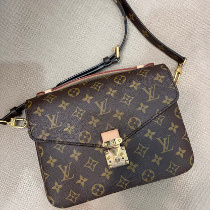 A Louis Vuitton monogram shoulder bag in brown coated canvas with gold-tone hardware, resting on a light beige textured fabric surface.
