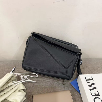 Black handbag and beige wallet on a gray surface with a Loewe box.