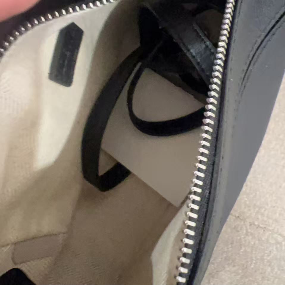 Close-up of a hand holding an open black leather bag with a visible brand logo.