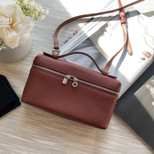 Brown leather handbag on a wooden surface with flowers and jewelry box.