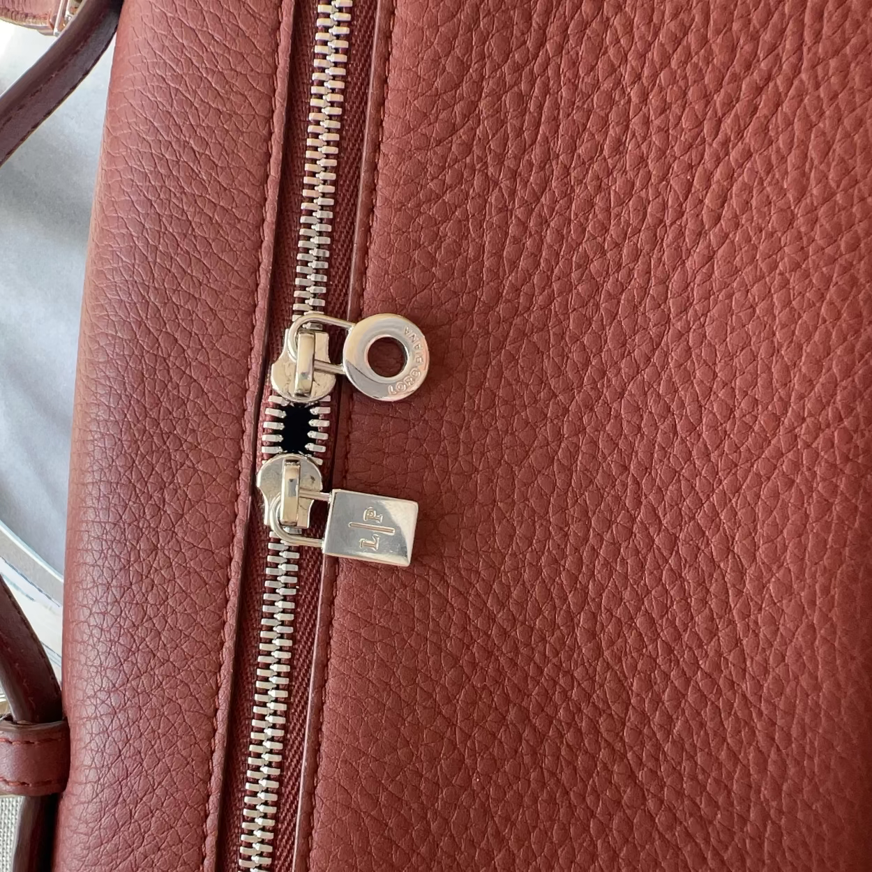 Close-up of a brown leather bag with a zipper and visible brand logo.