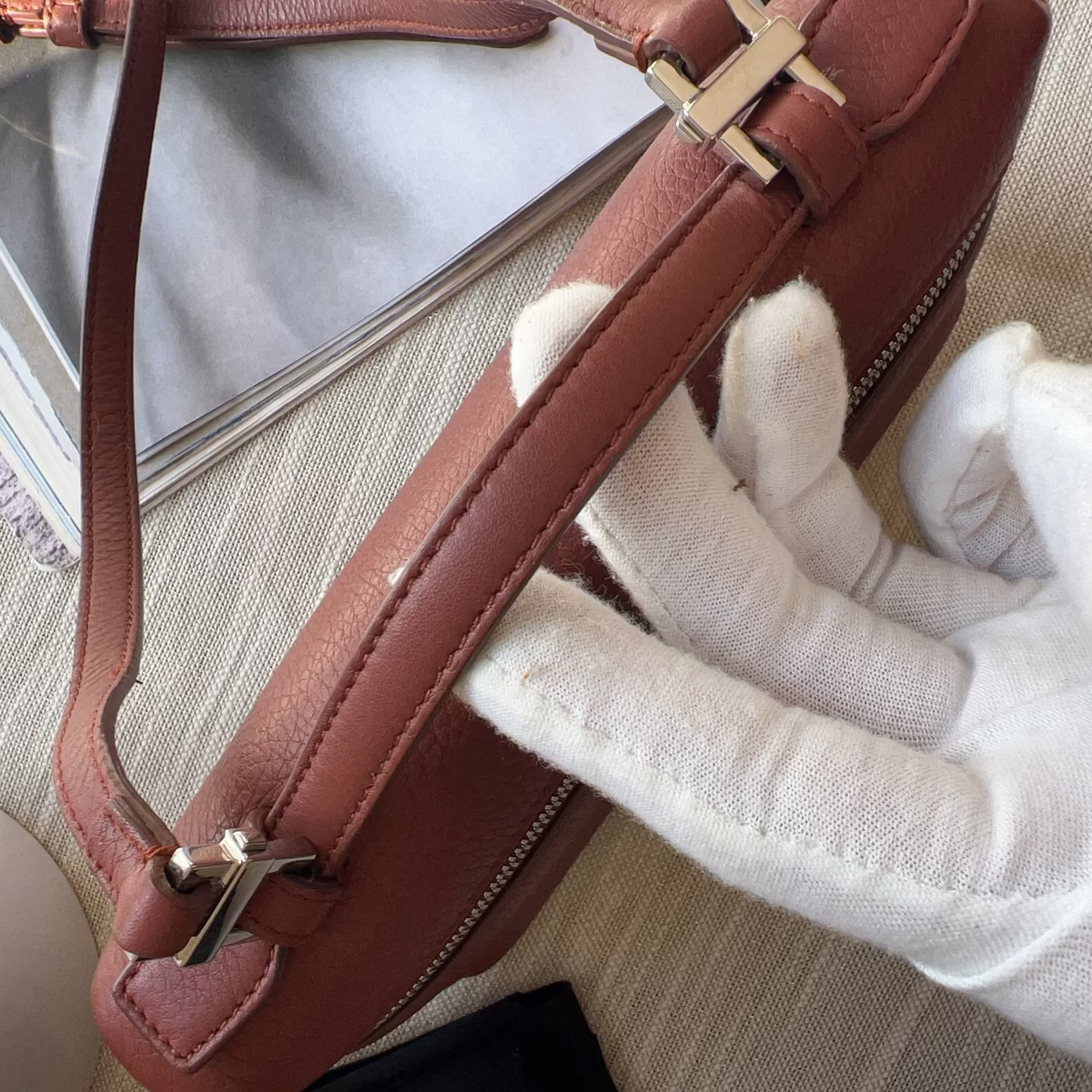 Brown handbag with gold hardware held by a gloved hand on a textured surface.