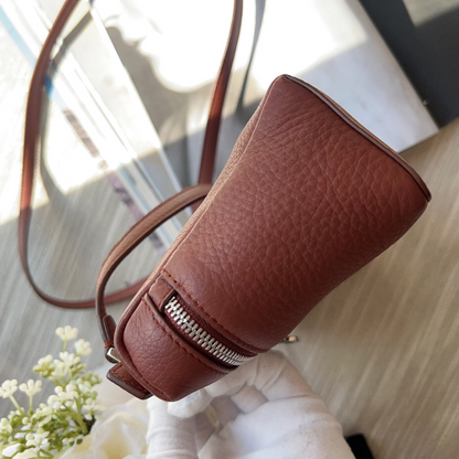 Brown leather pouch with a zipper on a light wooden surface.