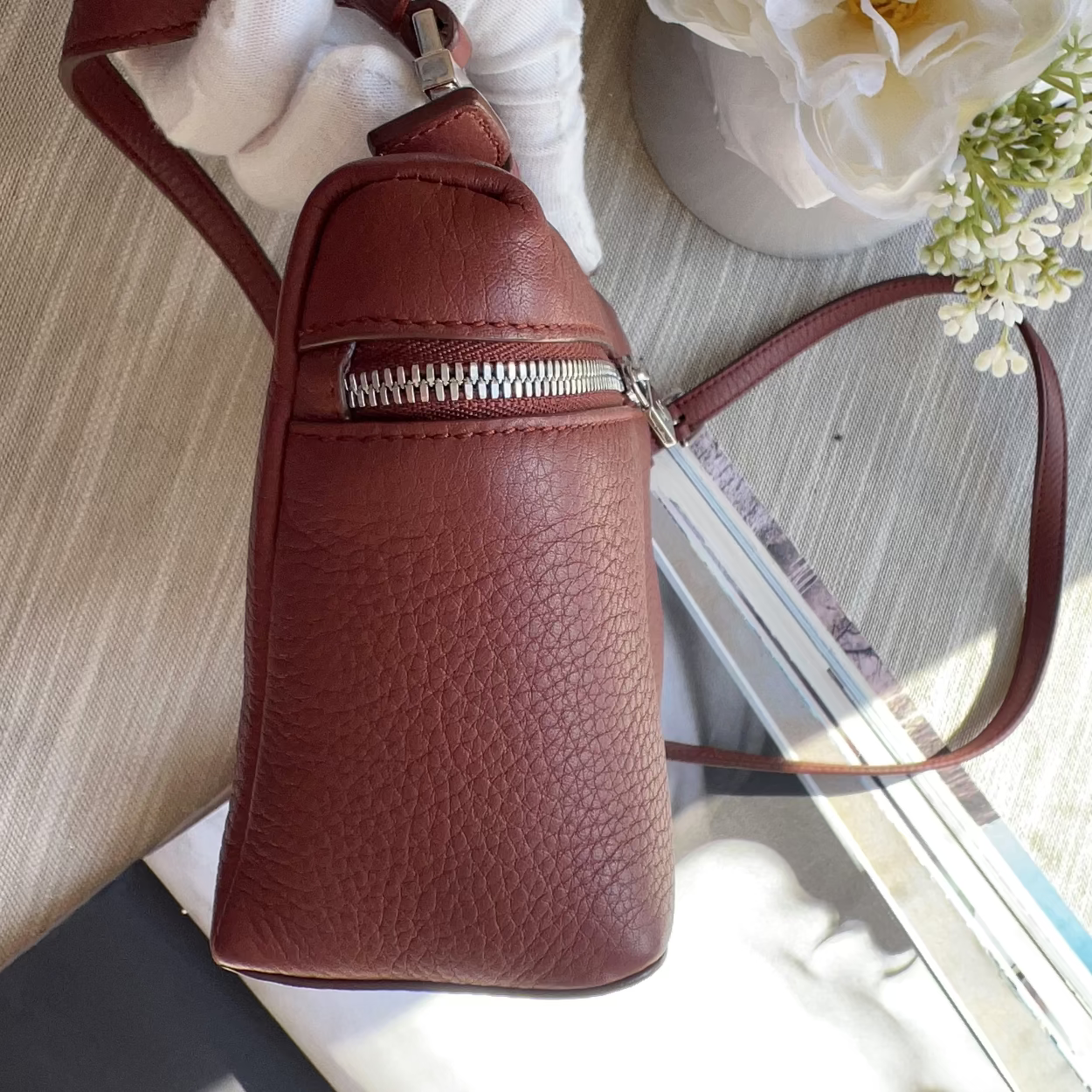 Brown leather handbag with a white flower on a wooden surface