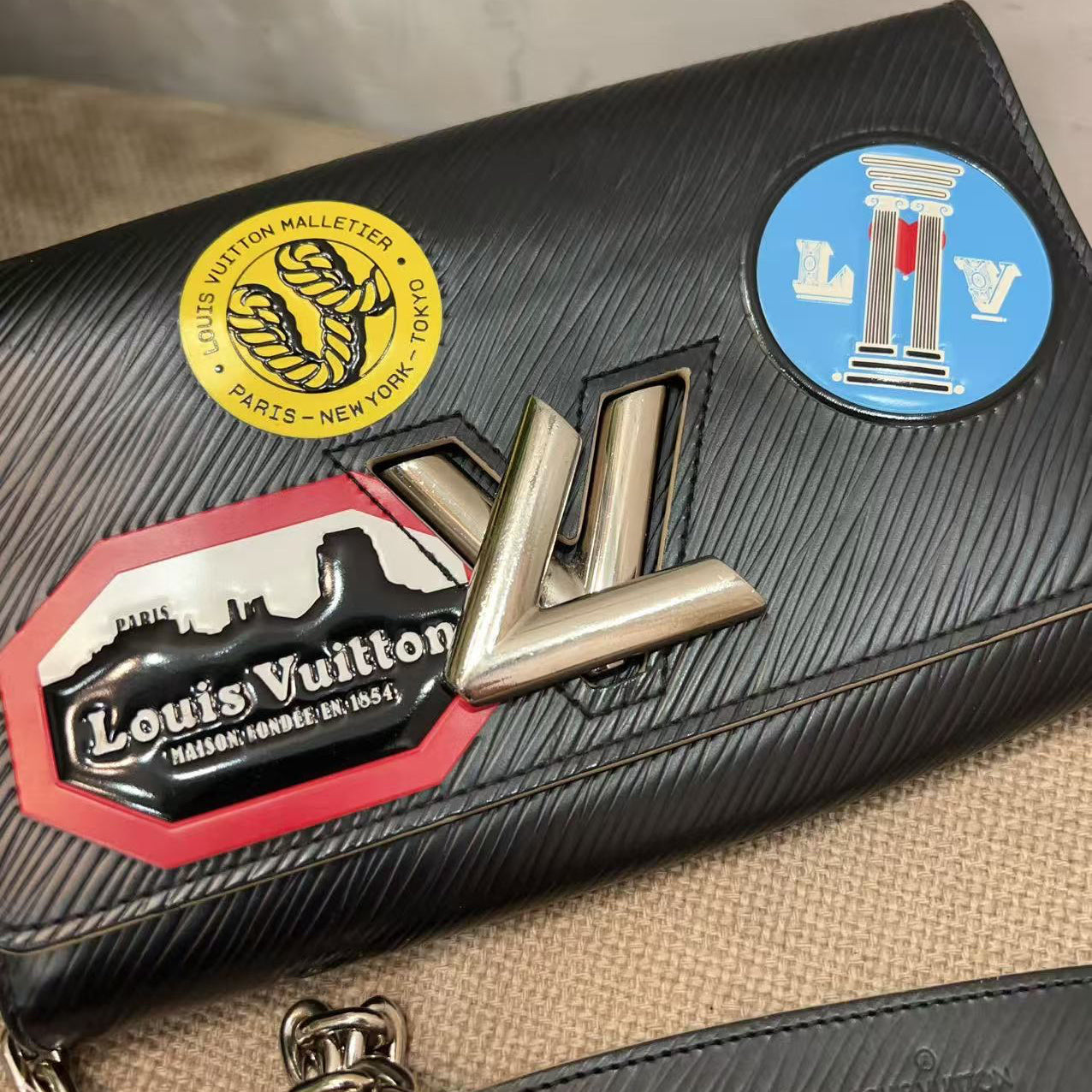 Black Louis Vuitton wallet with multiple brand stickers on a beige surface