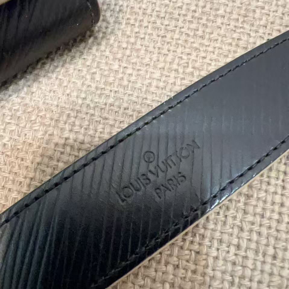 Close-up of a black leather strap with Louis Vuitton branding on a textured beige background.
