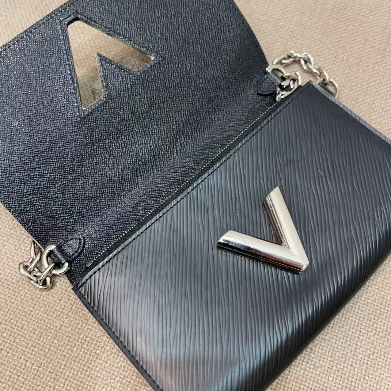 Black handbag with silver 'V' logo on a beige surface