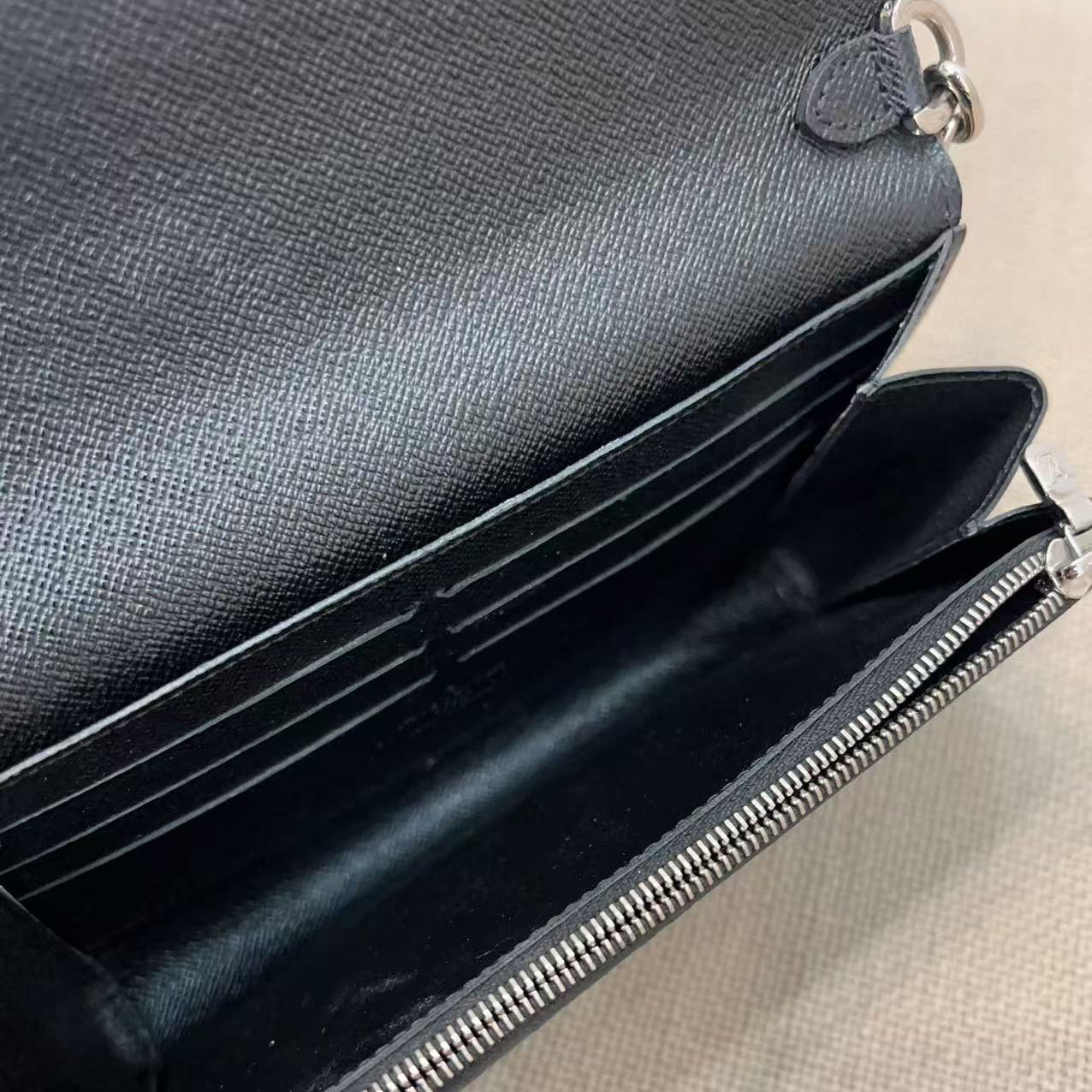 Black leather handbag with a zipper on a light brown surface