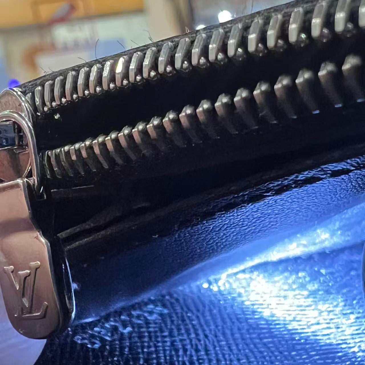 Close-up of a black leather wallet with a silver zipper, featuring a brand logo.