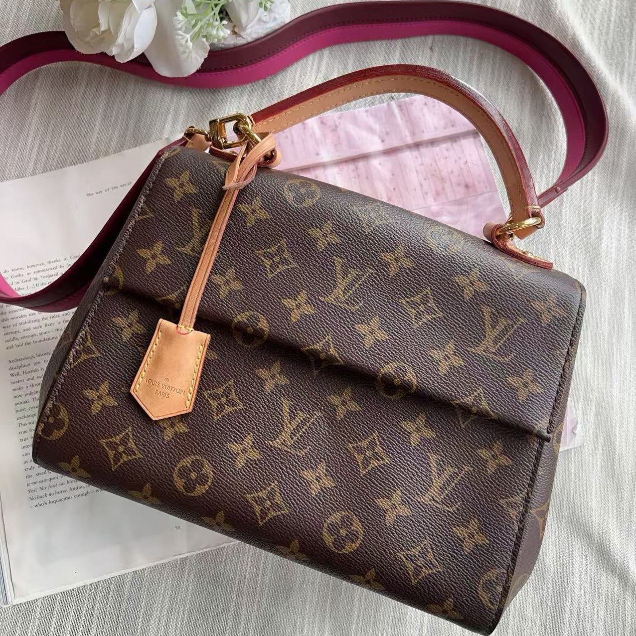 Designer handbag with monogram pattern on a textured surface with flowers.