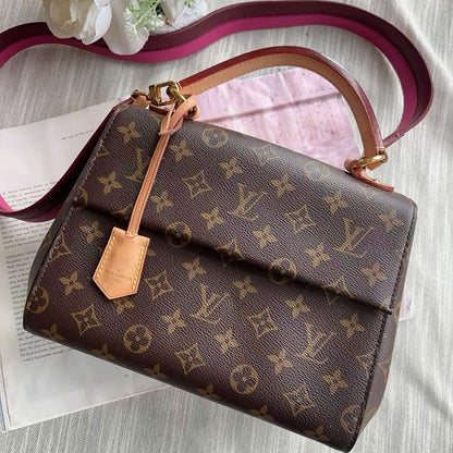 Designer handbag with monogram pattern on a textured surface with flowers.