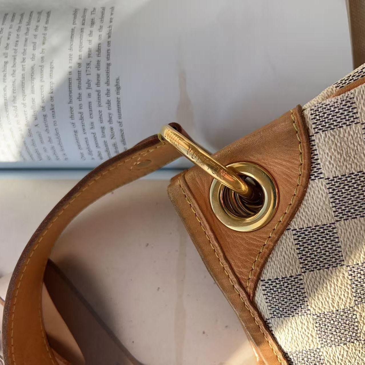Designer handbag with checkered pattern and gold hardware on a surface with an open book.