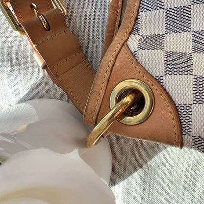 Close-up of a handbag with brown leather strap and gold hardware on a checkered fabric background.
