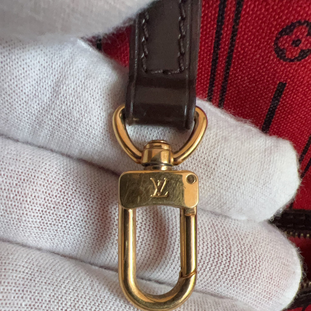 Gold keychain with Louis Vuitton logo on a white glove against a red plaid background