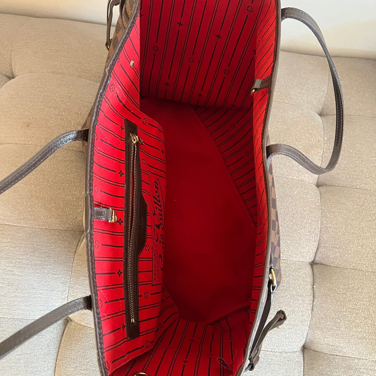 Red handbag with black interior lining on a beige sofa