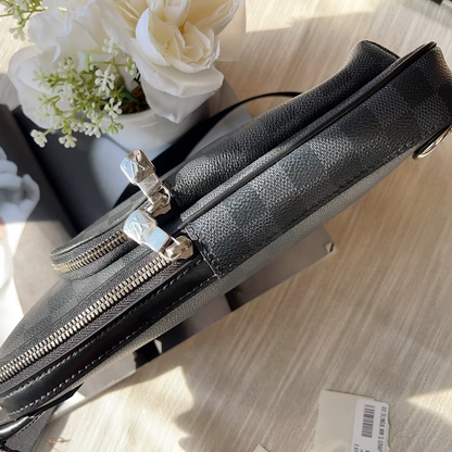 Black leather handbag with silver zippers on a light wooden surface with flowers in the background