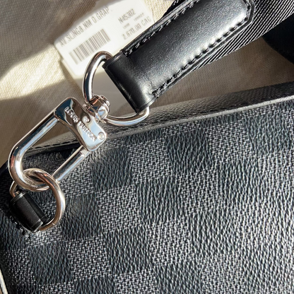 Close-up of a black leather bag with a silver clasp on a light wooden surface.