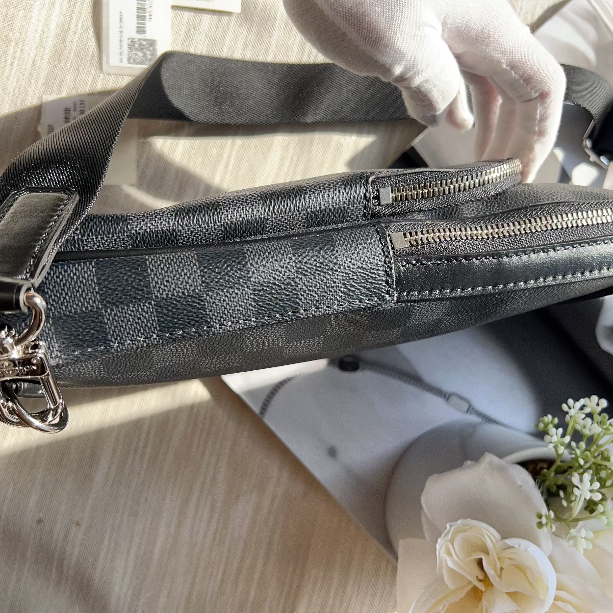 Gray checkered handbag with a zipper on a marble surface with flowers.