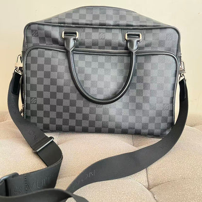 A Louis Vuitton shoulder bag in the signature Damier Graphite checkerboard pattern, featuring dark gray leather handles and a matching adjustable shoulder strap resting on a beige textured surface.