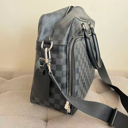 A Louis Vuitton shoulder bag in the Damier Graphite checkered canvas, shown from a side angle on a beige tufted sofa. The bag features silver-tone hardware, a black leather handle, and a matching black shoulder strap with the brand name debossed.