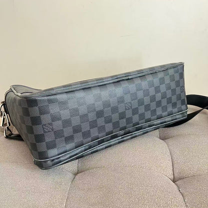 A Louis Vuitton shoulder bag in the Damier Graphite canvas, featuring a dark gray and light gray checkerboard pattern, resting on a beige tufted sofa.