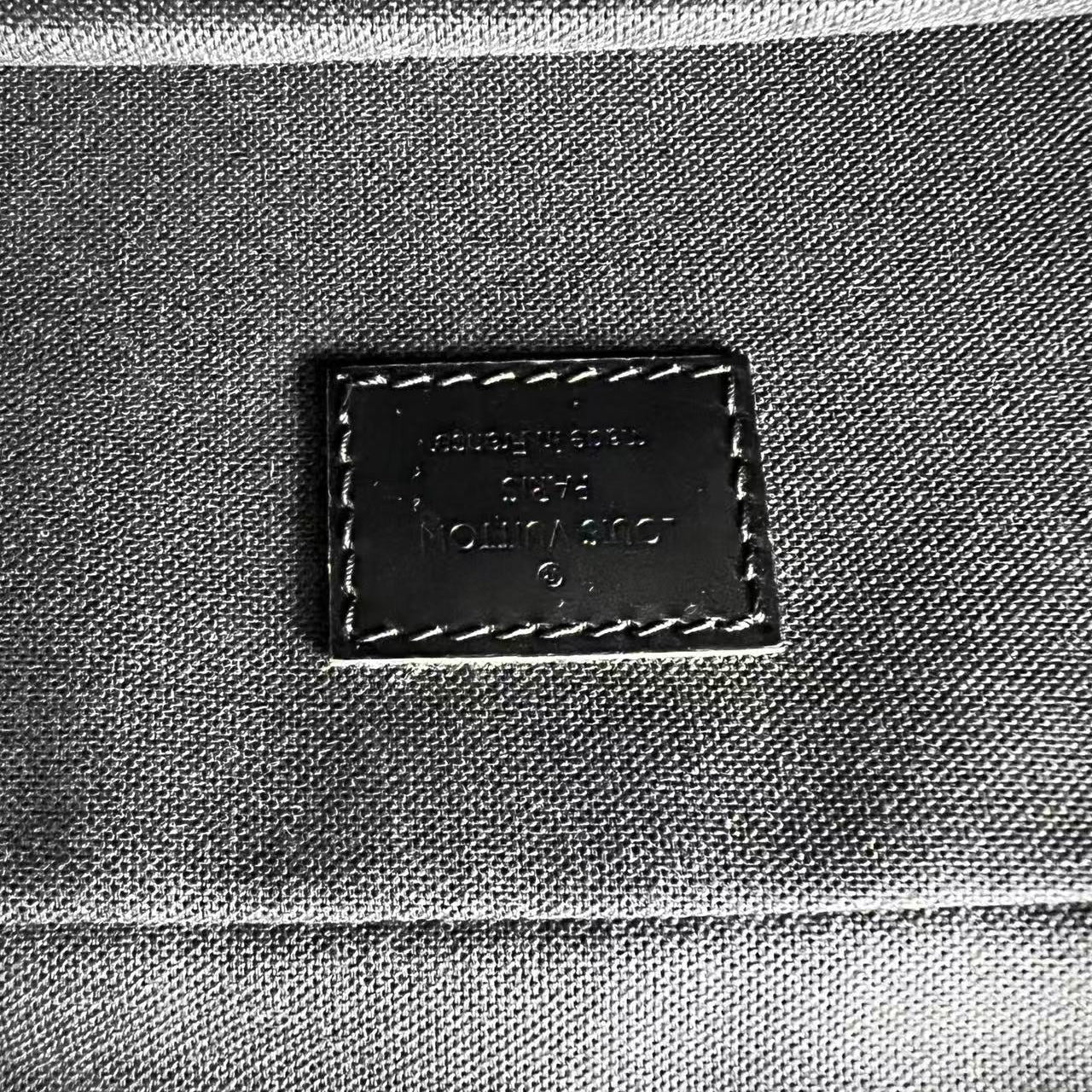 Close-up of a dark brown leather brand patch on a gray canvas fabric surface, with visible stitching around the patch.
