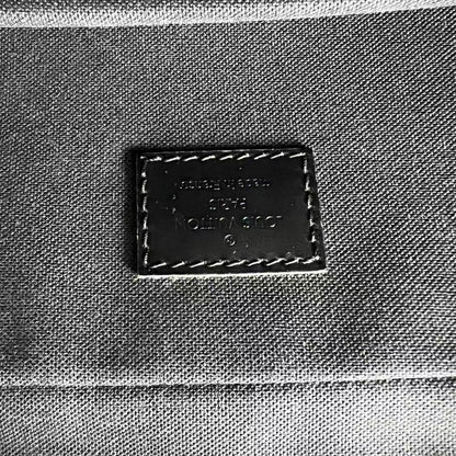 Close-up of a dark brown leather brand patch on a gray canvas fabric surface, with visible stitching around the patch.