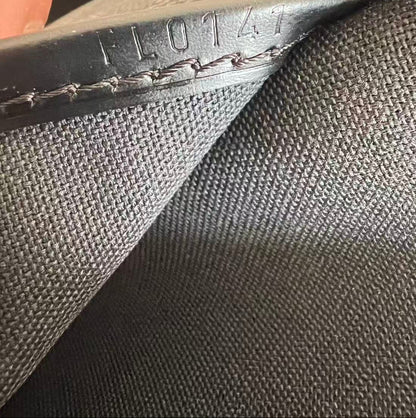 Close-up detail shot of a dark gray canvas and black leather bag, showing a silver zipper, stitched leather trim, and embossed numbers '110741' on the leather tab.