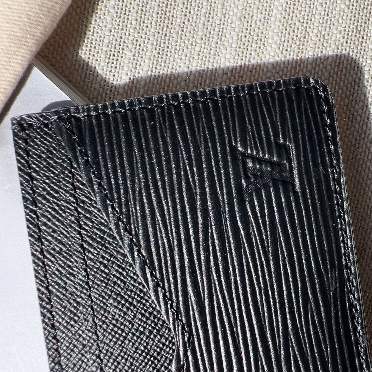 Black textured wallet with a brand logo on a beige fabric background