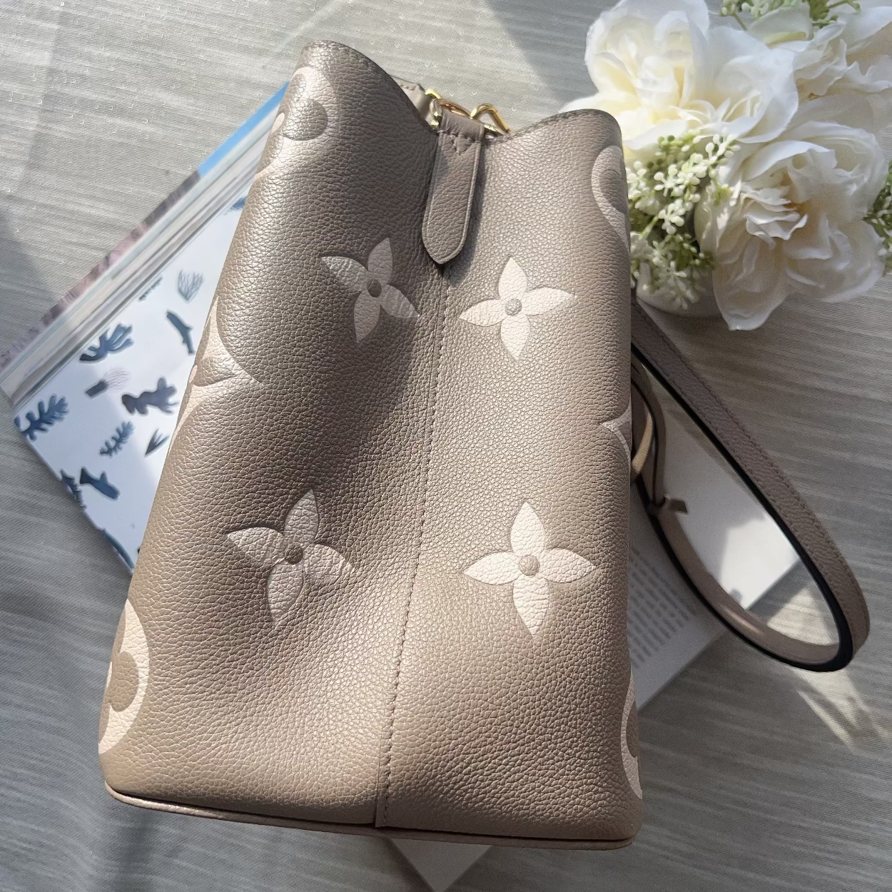 Designer handbag with floral embossing on a light wooden surface with flowers.