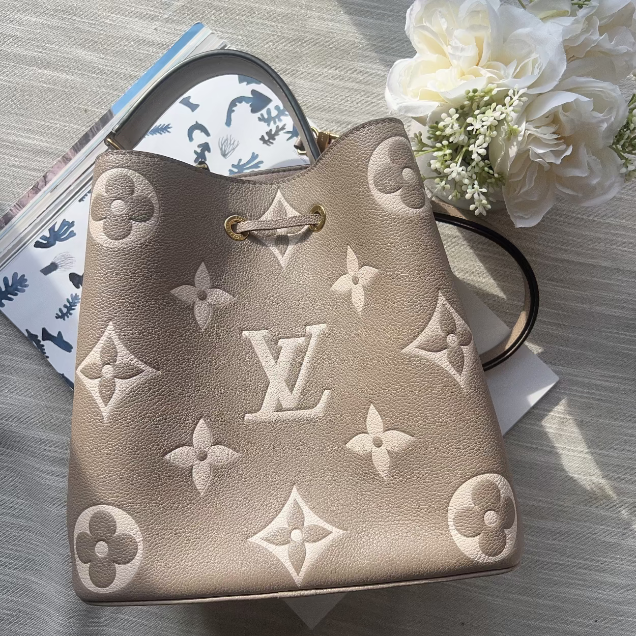 Designer handbag with monogram pattern on a textured surface with flowers.