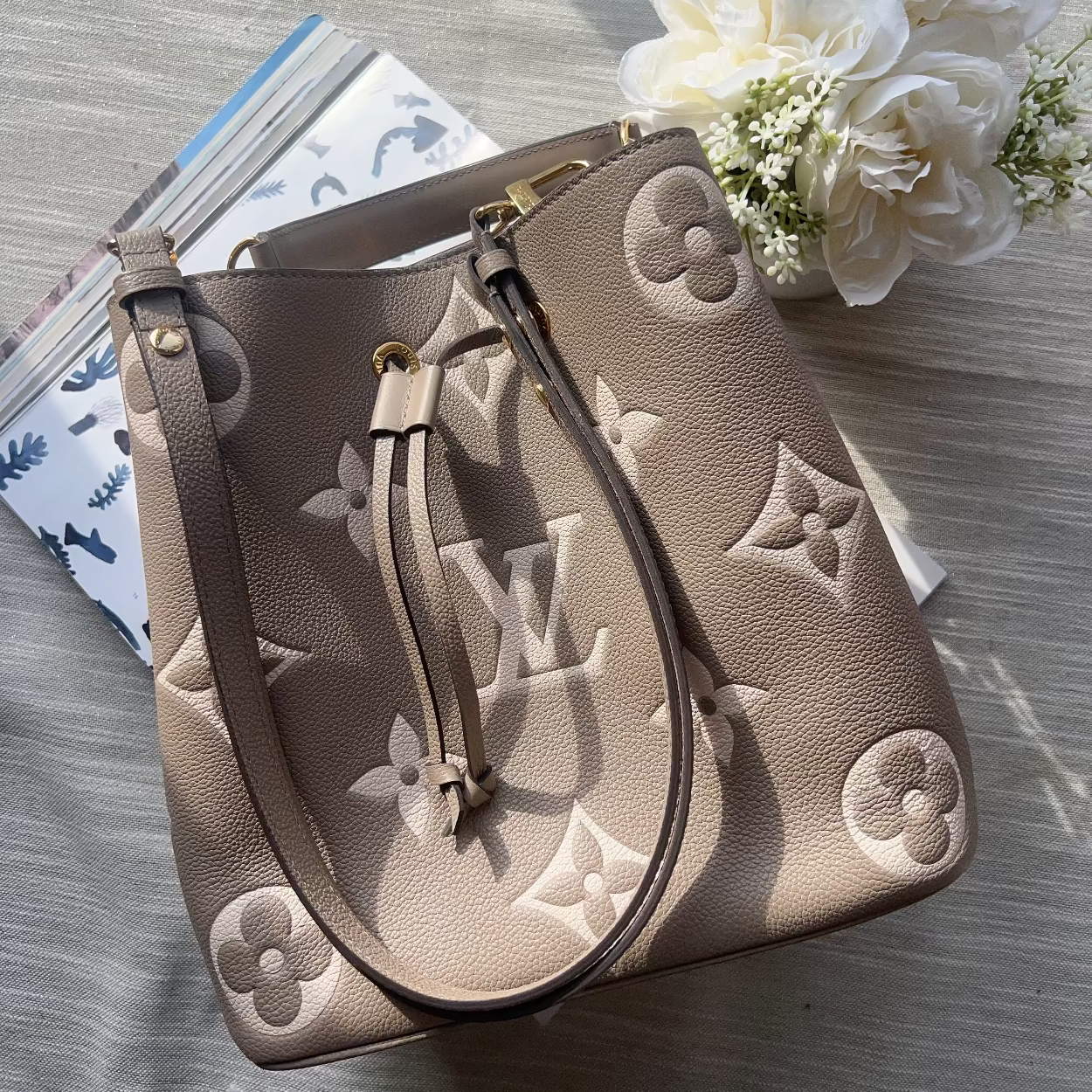Beige handbag with floral patterns on a light wooden surface with flowers.