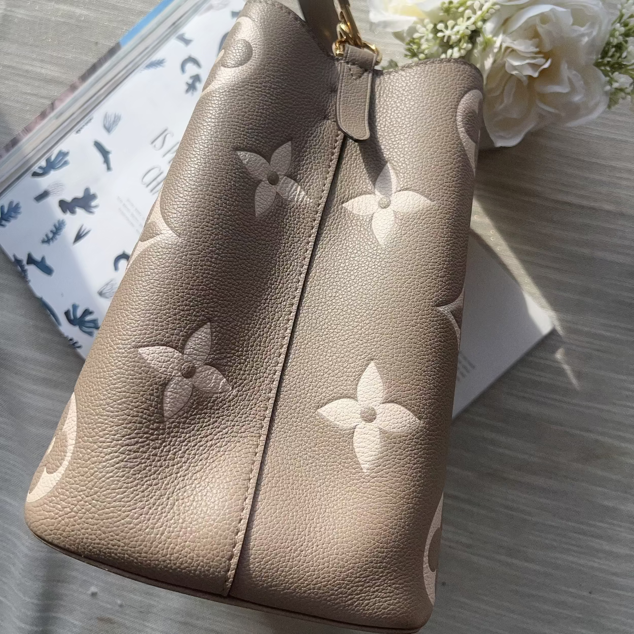 Beige handbag with floral patterns on a textured surface with flowers.