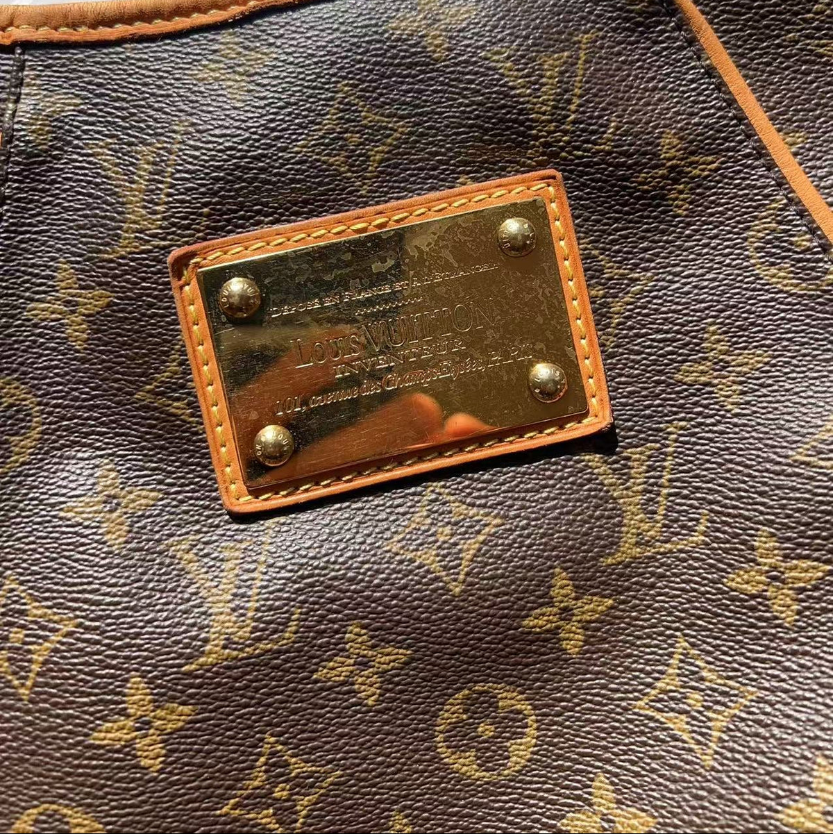Close-up of a Louis Vuitton monogram canvas bag with tan leather trim and a gold-tone metal plaque on the front.