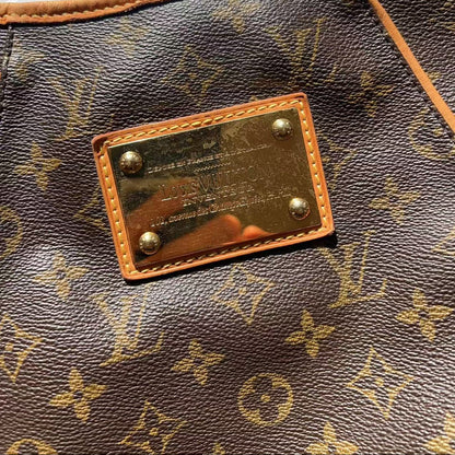 Close-up of a Louis Vuitton monogram canvas bag with tan leather trim and a gold-tone metal plaque on the front.