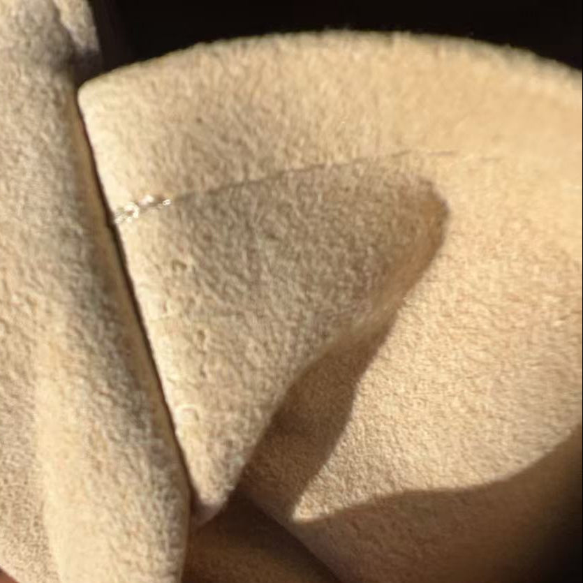 A close-up of a beige suede or faux-suede material being held by a hand, showing the soft texture and folded edges under warm lighting.