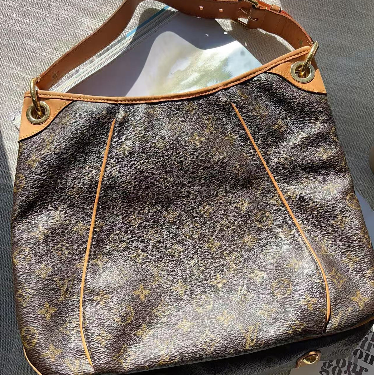 A Louis Vuitton monogram shoulder bag in brown coated canvas with tan leather trim and gold-tone hardware, photographed on a light gray textured surface.