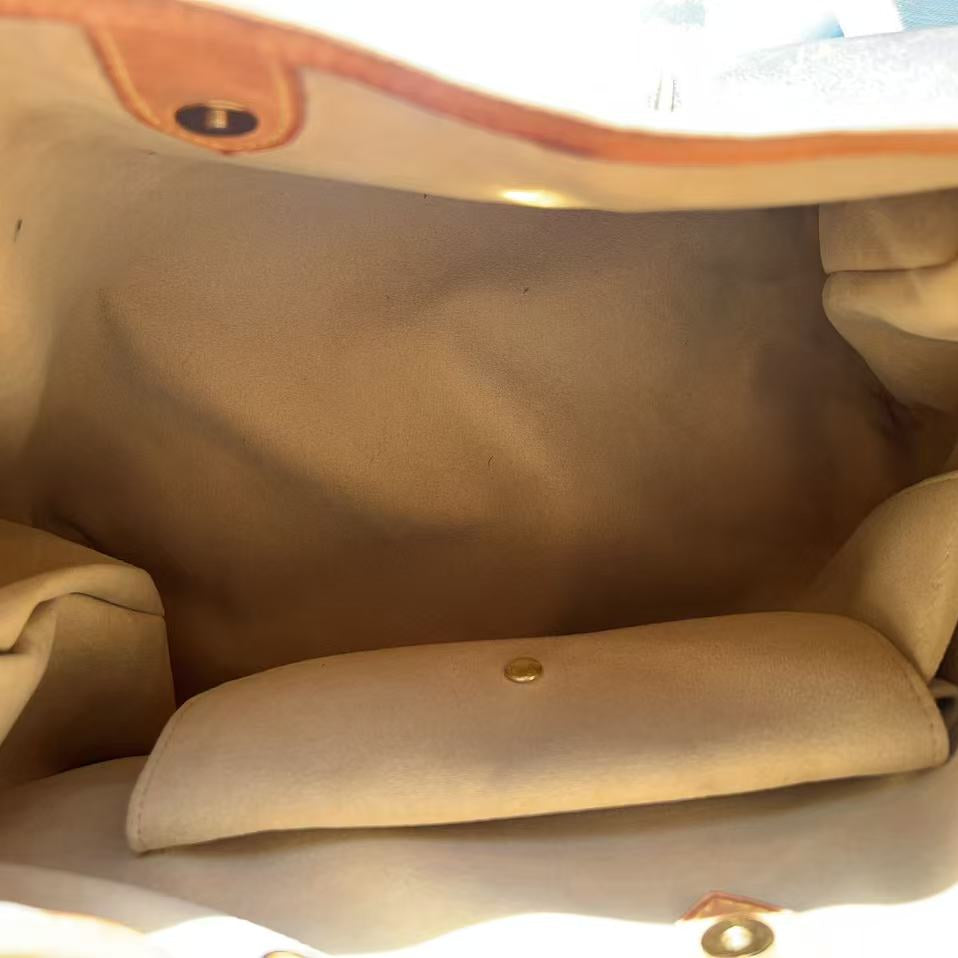 Close-up view inside a beige canvas or fabric bag, showing the interior lining, a small matching pouch or organizer, and tan leather trim with metal hardware.