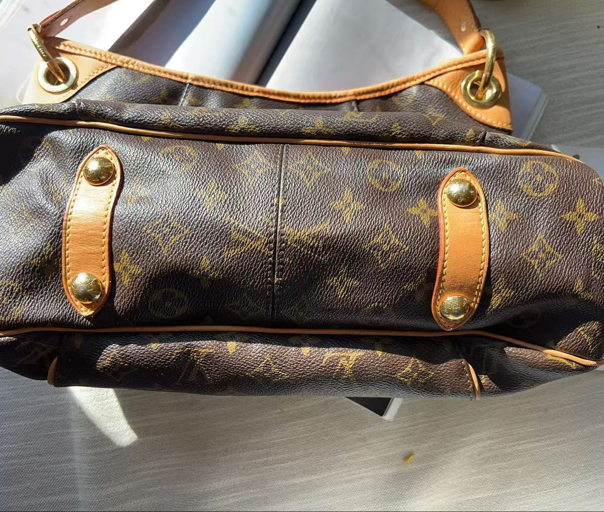 A Louis Vuitton monogram shoulder bag in brown coated canvas with tan leather trim and gold-tone hardware, photographed from above on a light surface.